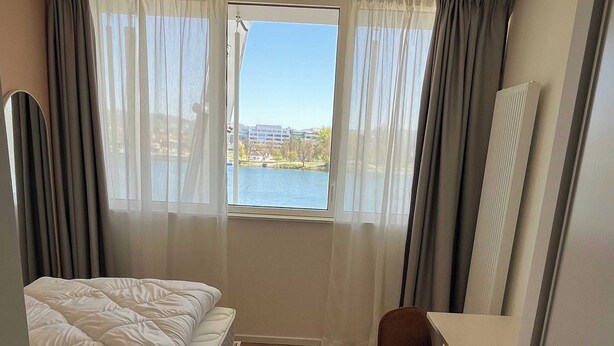 A hotel room with a bed, a desk, and a view of a lake. - Comfort Studio in a Premium Residence- Sport/cinema (Huningue)