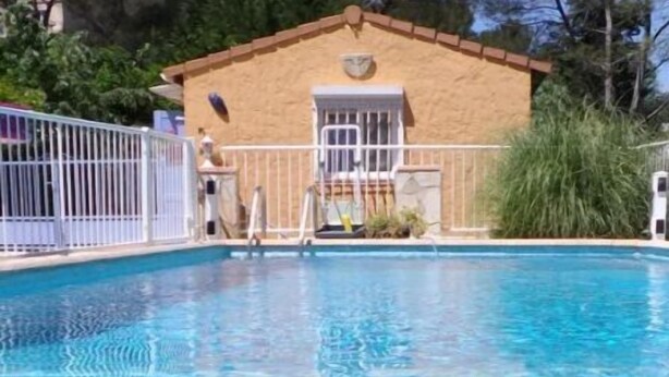 Une piscine d’un bleu éclatant, entourée d’une clôture blanche, un petit bâtiment avec une porte et des fenêtres, et de la verdure en arrière-plan.