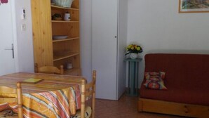 Une pièce avec une bibliothèque en bois, un canapé rouge, une petite table recouverte d’une nappe à rayures et un climatiseur fixé au mur.