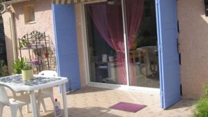 Un patio couvert avec une table et des chaises, une porte-fenêtre coulissante et un petit jardin agrémenté de plantes en pot.