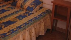Une chambre à coucher avec un lit, une petite table de chevet en bois et une fenêtre avec des rideaux.