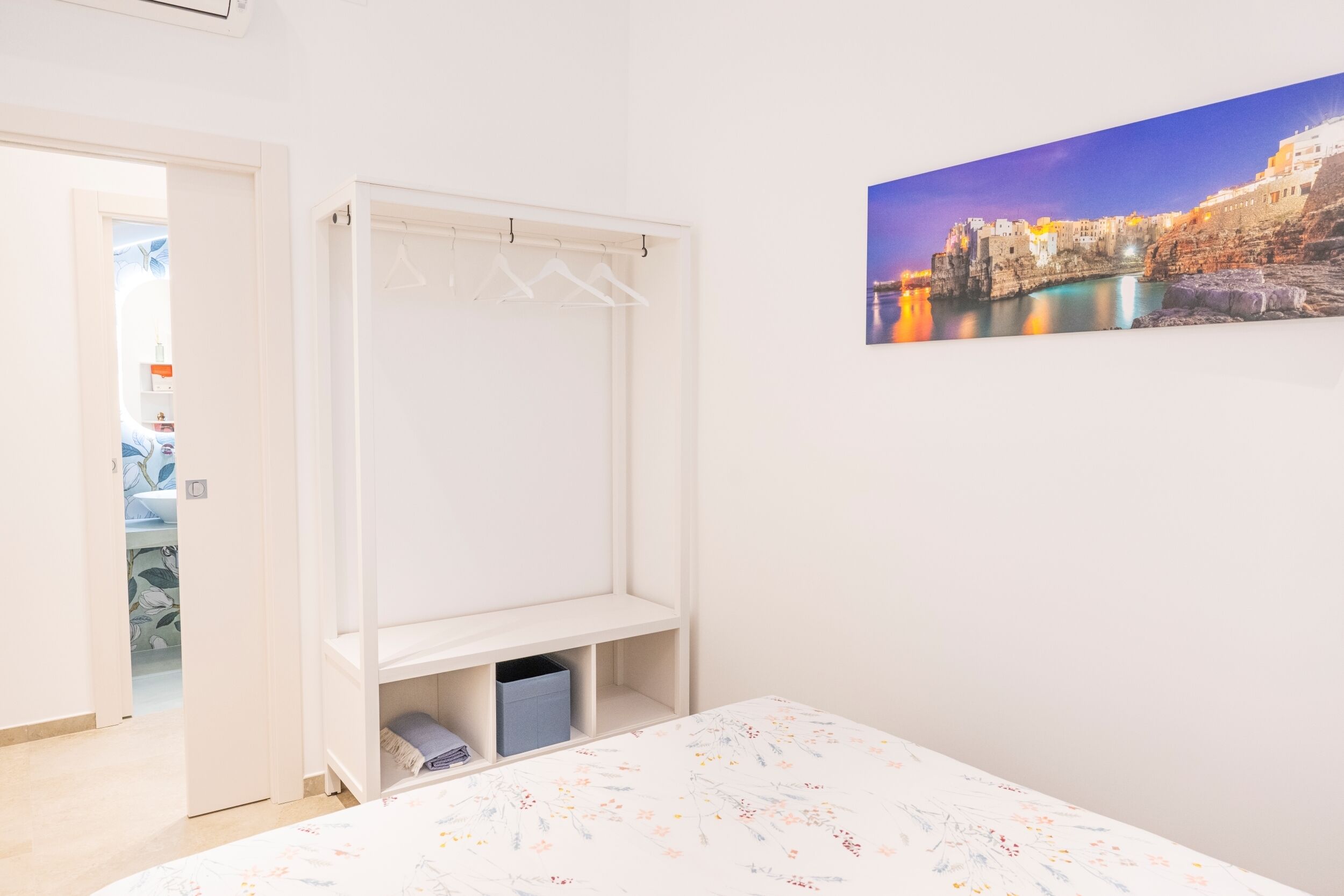 A bedroom with a bed, a wardrobe, a hanging closet, and a cityscape painting on the wall.