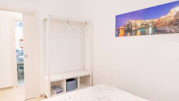 A bedroom with a bed, a wardrobe, a hanging closet, and a cityscape painting on the wall.