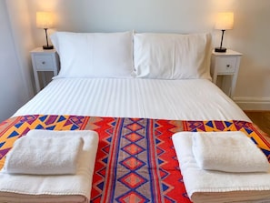 Una cama con sábanas blancas, dos mesitas de noche con lámparas y una manta de colores con estampado geométrico.