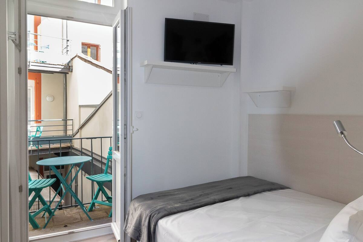 Ein Schlafzimmer mit Bett, einem an der Wand montierten Fernseher und einem Balkon mit Tisch und Stühlen.