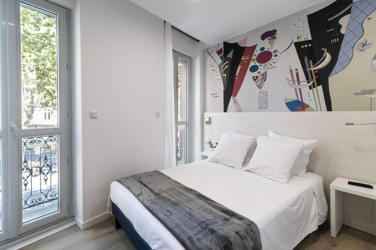 Ein modernes Schlafzimmer mit einem großen Bett, einem weißen Nachttisch und einem Wandgemälde.
