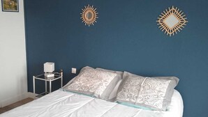 Un dormitorio con una cama, dos objetos decorativos en la pared con forma de sol, una mesita de noche con lámpara y almohadas estampadas.