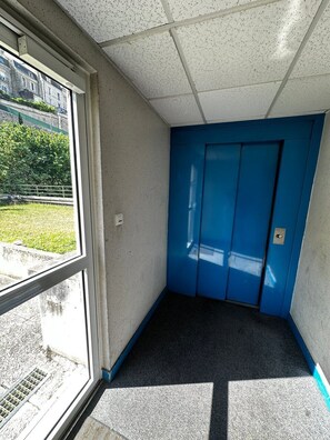 Ein Eckzimmer mit Fenster, ein blauer Aufzug und ein gemusterter Boden.
