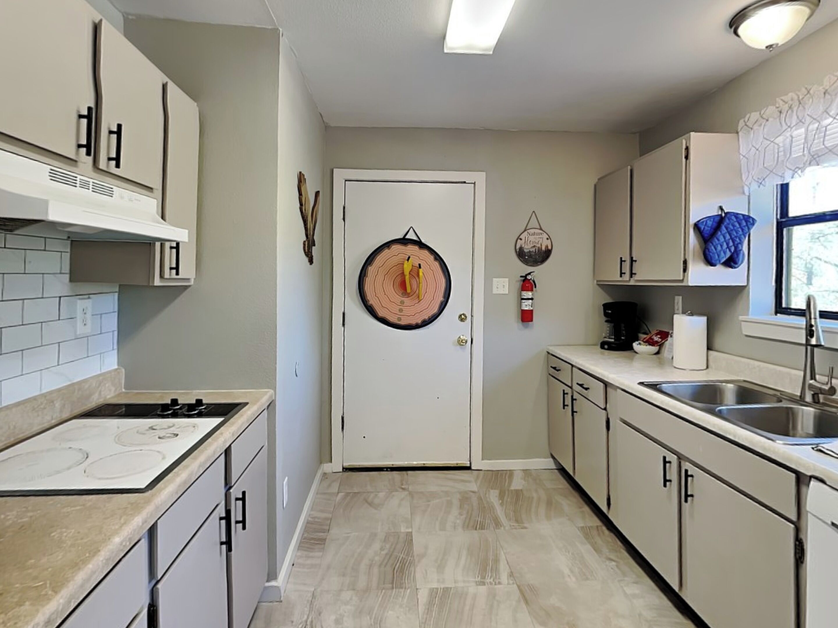 A kitchen with a stove, cabinets, a sink, and a door with a circular decoration.