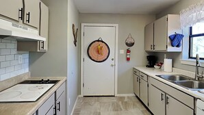 A kitchen with a stove, cabinets, a sink, and a door with a circular decoration. - Knotty Pines Cabin by Ruidoso Vacation Rentals (Ruidoso)
