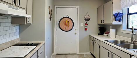 A kitchen with a stove, cabinets, a sink, and a door with a circular decoration.
