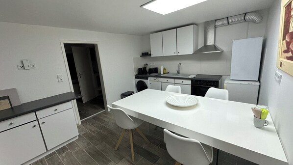 Una cocina compacta con armarios blancos, una mesa de comedor y un refrigerador.