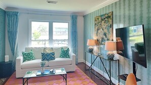 A living room with a white sofa, a coffee table, a TV, and a patterned rug. - Jamaica Palms Oasis by Ryson Vacation Rentals (Galveston)