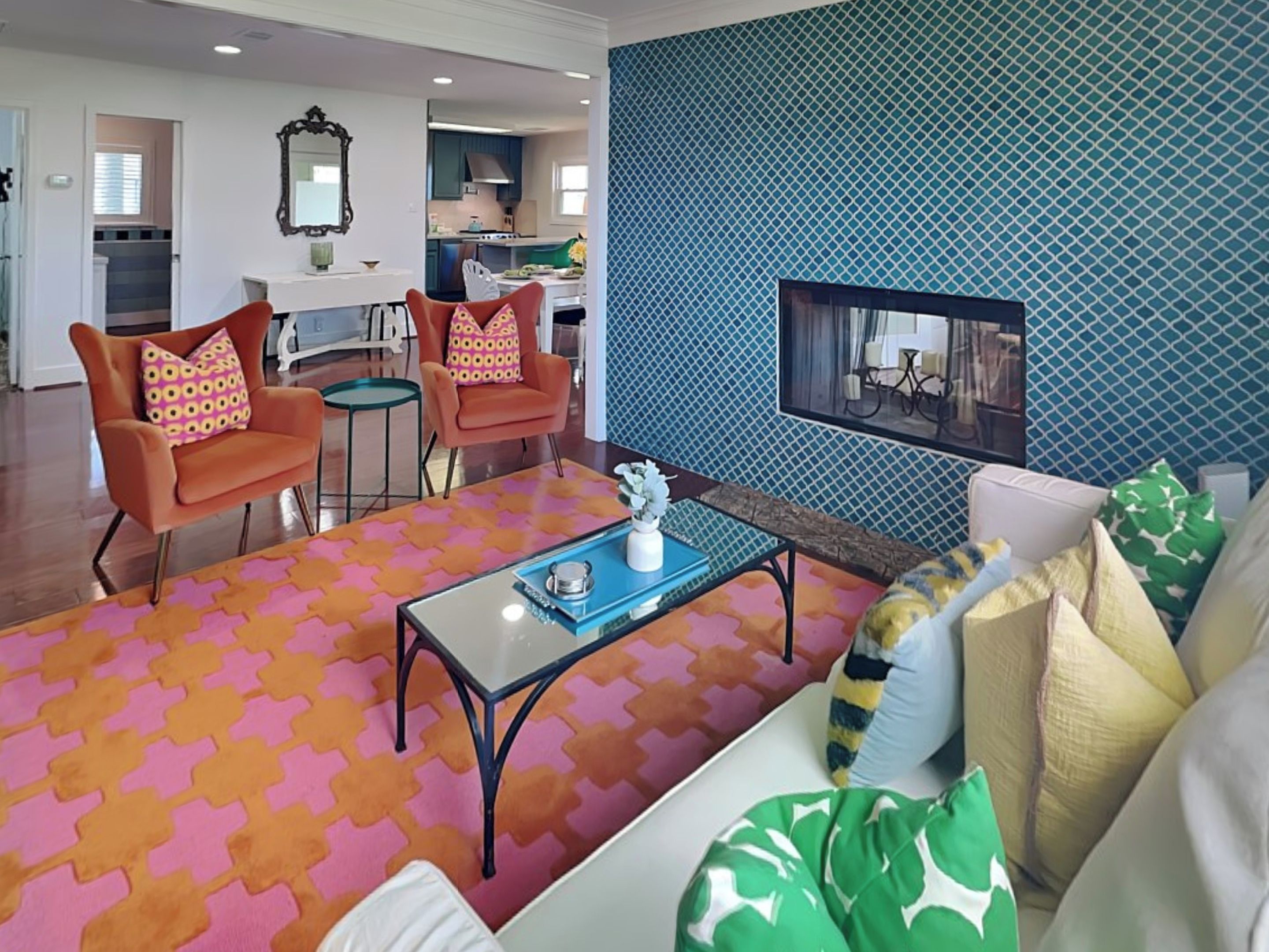 A modern living room with orange armchairs, a glass coffee table, and a patterned rug.
