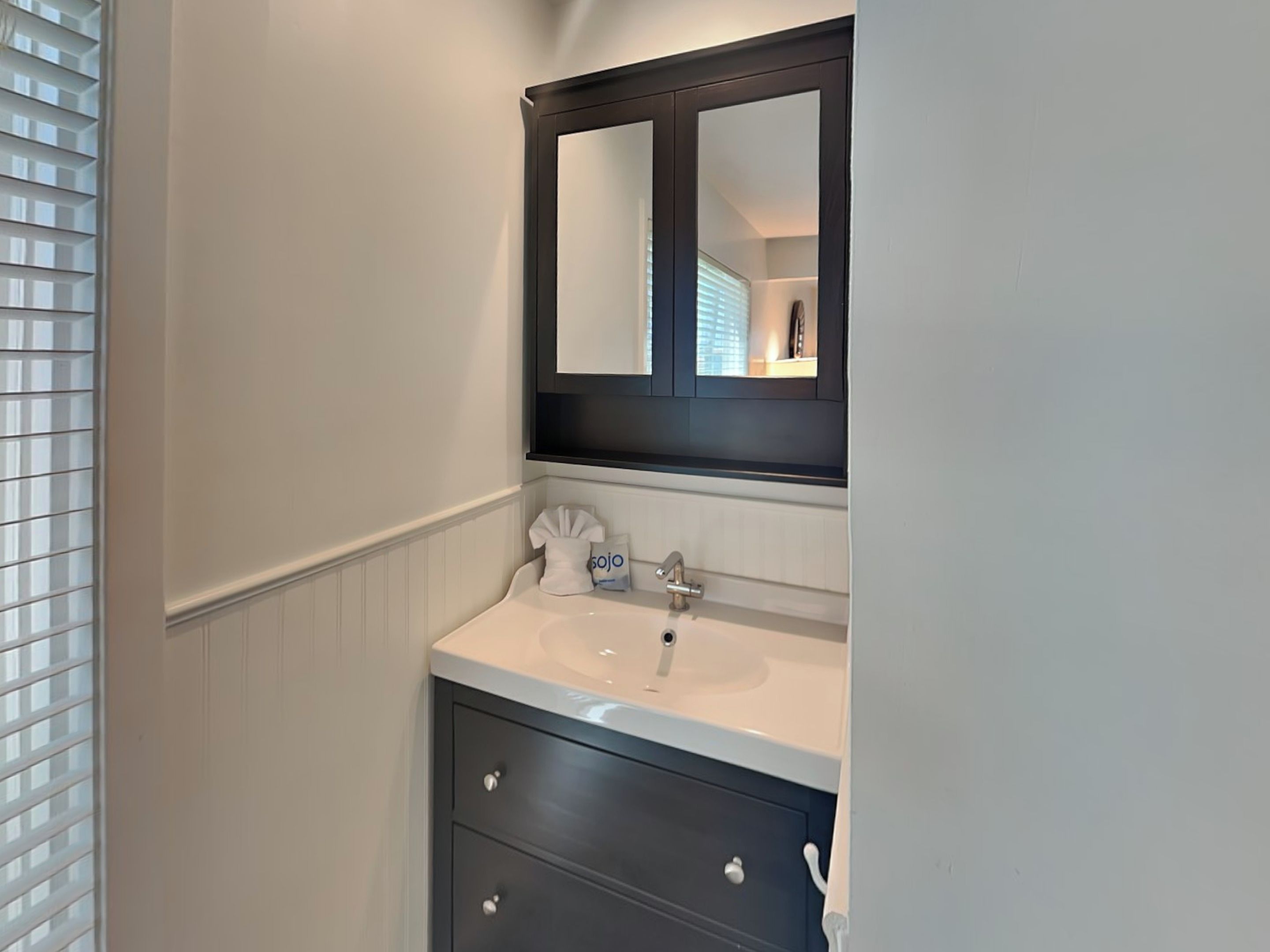 Une salle de bain avec un lavabo blanc, un meuble-lavabo foncé et un miroir au-dessus du lavabo.