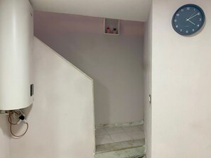 Una escalera con un reloj fijado a la pared y un pequeño estante con adornos.