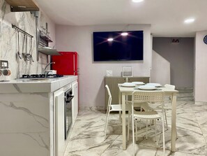 Ett modernt kök med en gasspis, röda skåp och en tv som är monterad ovanför ett matbord med vita stolar.