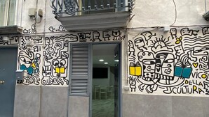 A building with a metal balcony, a door with a window, and walls adorned with black and white graffiti.