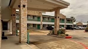A motel with a covered parking area, multiple-story buildings, and a green entrance. - Garden Inn Express (Humble)