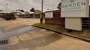 A sign for Garden Inn Express with a parking lot and buildings in the background. - Garden Inn Express (Humble)