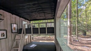 Un chalet rustique avec un lit en mezzanine, une échelle en bois et une fenêtre donnant sur une forêt.