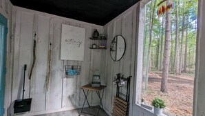 L’intérieur d’un chalet rustique, avec des murs en bois, une petite table sur laquelle se trouve une bouilloire, un miroir et une fenêtre donnant sur une forêt.
