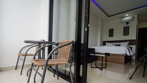 A hotel room with a bed, a small table, two wicker chairs, and a glass door leading to a balcony.