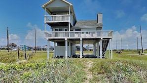 A two-story beachfront house with a balcony, a covered porch, and a small staircase leading to the upper level. - Whispering Sands Beachfront by Ryson Vacation Rentals (Galveston)