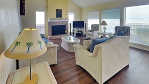 A living room with wicker furniture, a fireplace, and a television. - Whispering Sands Beachfront by Ryson Vacation Rentals (Galveston)