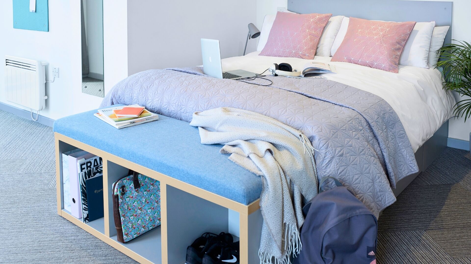 Ein ordentlich eingerichtetes Schlafzimmer mit einem Bett, einem Nachttisch und einer Bank mit Büchern und einer Tasche.