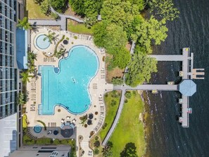 Vue aérienne d’un complexe hôtelier doté d’une grande piscine, d’un quai et d’une végétation luxuriante.