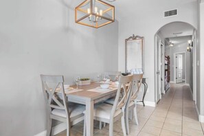 A dining area with a wooden table, white chairs, a hexagonal light fixture, and a mirror on the wall.