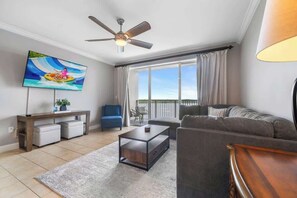 A living room with a ceiling fan, a flat-screen TV, a sofa, a coffee table, and a view of the outdoors.