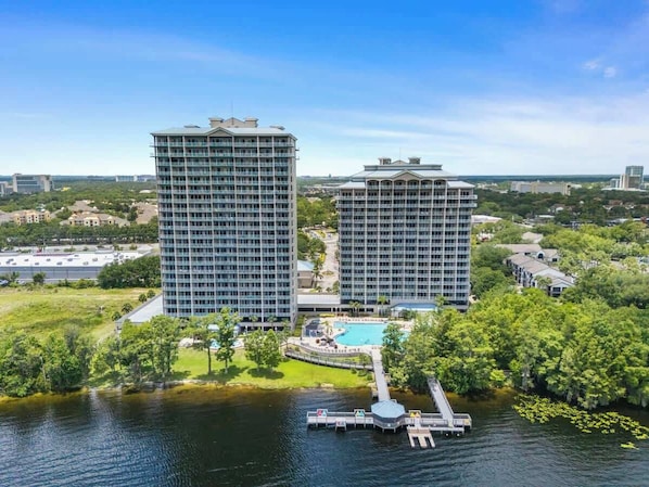 A high-rise hotel with a pool and dock, surrounded by greenery and water.