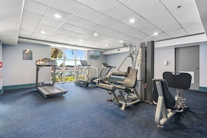 Uma academia com equipamentos de cardio, aparelhos de musculação e um banco.
