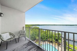 Un balcon avec deux chaises, une piscine et une vue sur une étendue d’eau et la verdure.
