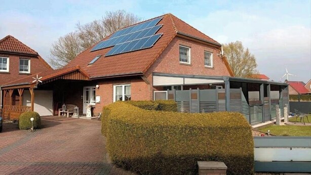 Una casa de ladrillo rojo, con paneles solares en el techo y un jardín delantero bien cuidado con seto.