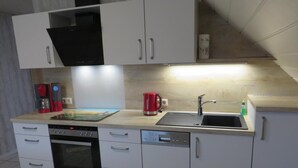Una cocina moderna con armarios blancos, horno integrado, lavavajillas, pileta y cafetera.