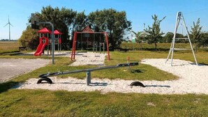 Un parque infantil con un tobogán rojo, columpios y un sube y baja.