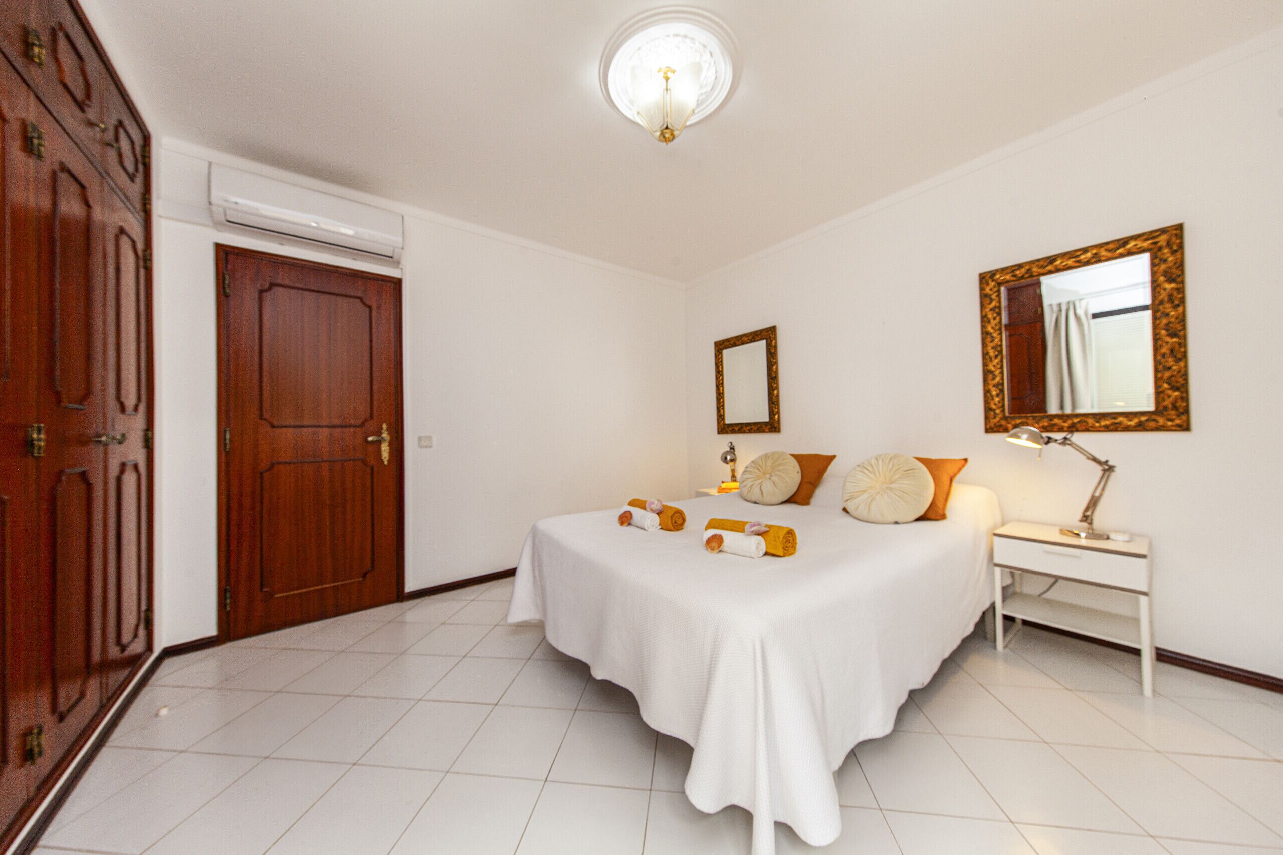 A bedroom with a bed, bedside table, lamp, and a mirror on the wall.