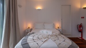 Un lit bien fait, recouvert d’une couverture à motifs, deux lampes de chevet, un extincteur et une porte, le tout dans une chambre d’hôtel.