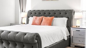 Una cama bien hecha con un cabecero capitonado, ropa de cama blanca y dos almohadas naranjas.