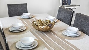 Una mesa de comedor con un centro de mesa decorativo, cuencos y platos blancos sobre un mantel con diseño geométrico.