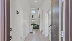 Un pasillo estrecho con paredes blancas y suelo de madera que conduce a una habitación con un sofá verde y una mesita.