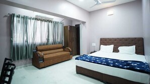 A bedroom with a bed, a sofa, a ceiling fan, and a window with curtains.