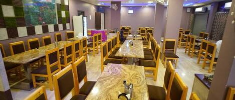 A restaurant with multiple tables and chairs, a large screen displaying an advertisement, and a counter area.