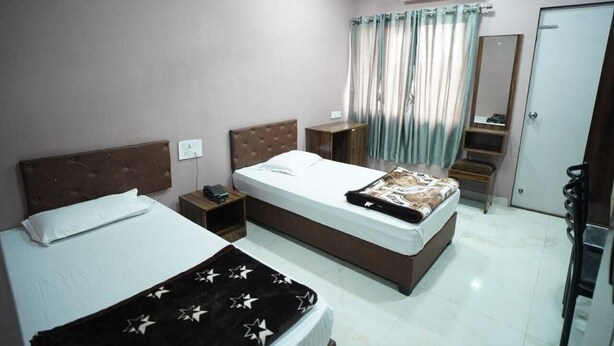 A hotel room with two beds, a bedside table, a mirror, a wardrobe, and an air conditioning unit.