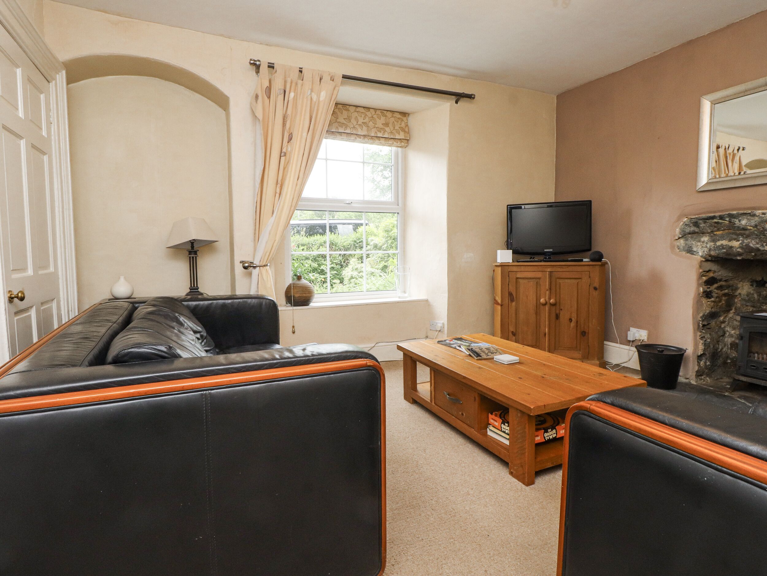 A living room with a sofa, a wooden table, a television, and a stone fireplace.
