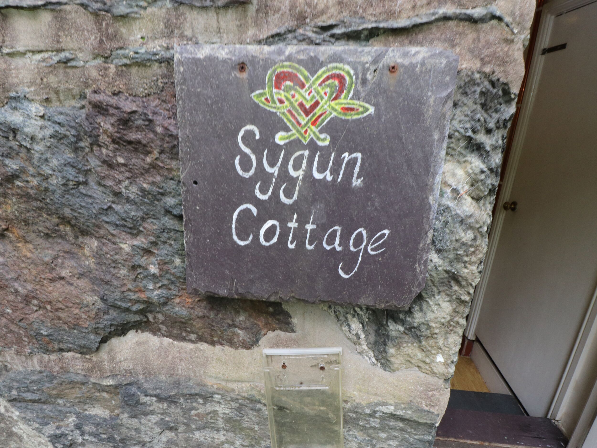 Uma placa de pedra com o texto "Sygun Cottage" e um emblema decorativo.