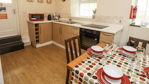 Cocina compacta con armarios de madera, microondas y lavamanos. Hay una mesa de comedor con platos y vasos.